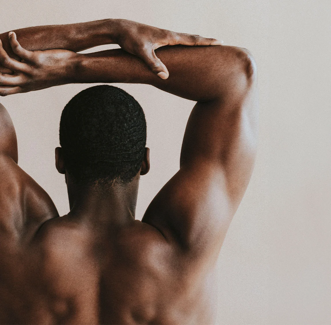 The back view of a muscular man stretching his arms over his head, showcasing his well-defined back and shoulders - Arm Lift at HIM Plastic Surgery