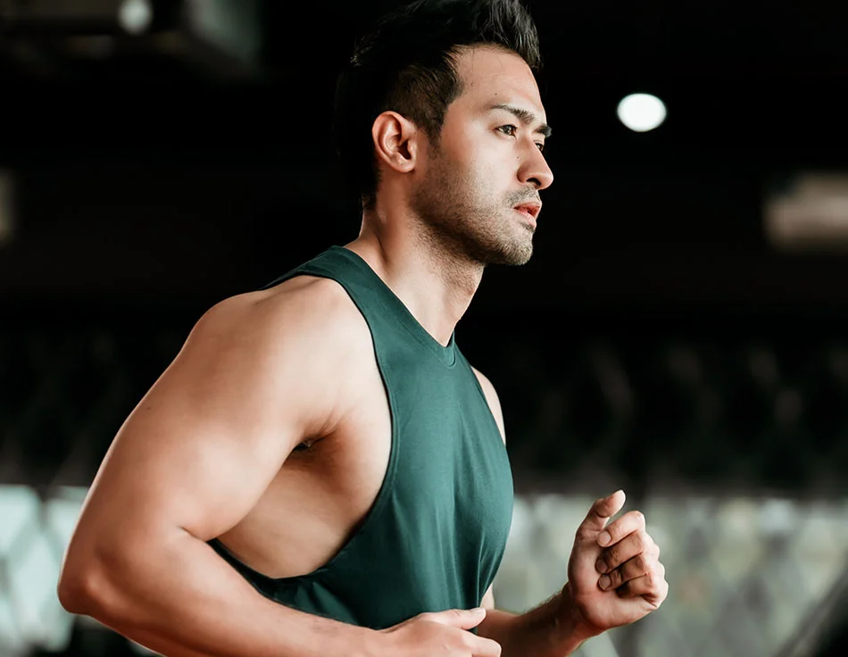 A man running indoors, wearing a green sleeveless top, with a focused expression - Body Lift Procedure at HIM Plastic Surgery