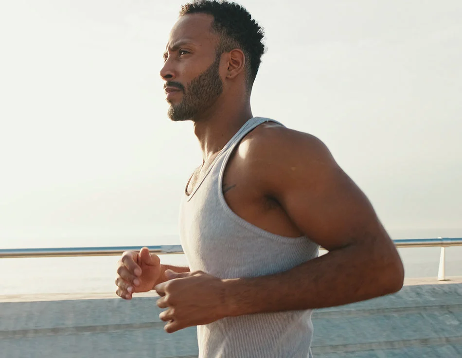 A man jogging by the beach in a gray tank top - Daddy Do Over at HIM Plastic Surgery