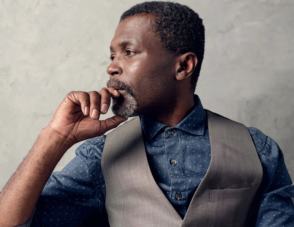 A thoughtful man in a vest and button-up shirt, resting his hand on his chin - Facelift at HIM Plastic Surgery