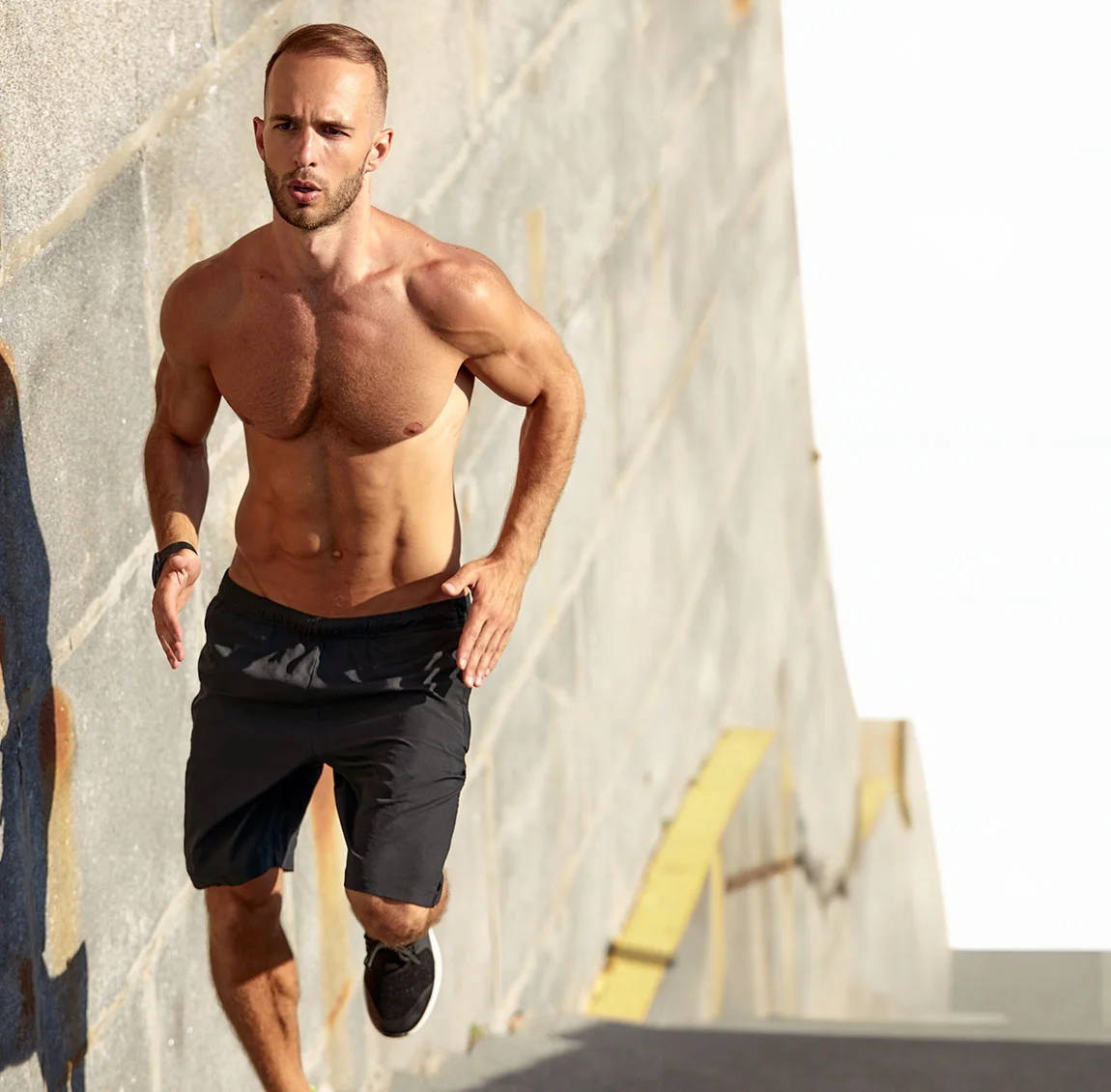 A shirtless, muscular man running up a concrete ramp in the sunlight - Liposuction at HIM Plastic Surgery