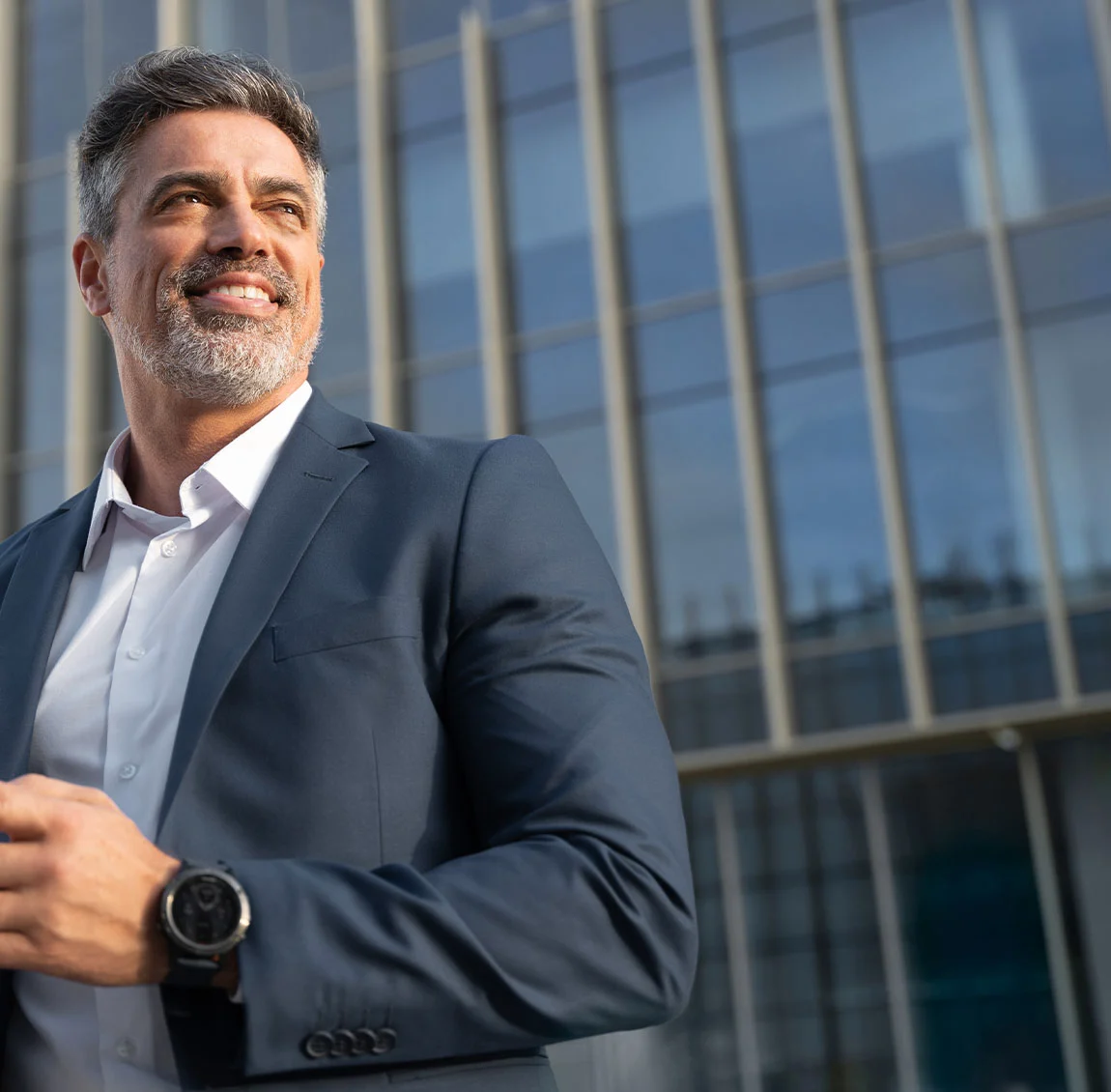 A man in a suit, standing agains a glass building - Revision Facelift at HIM Plastic Surgery