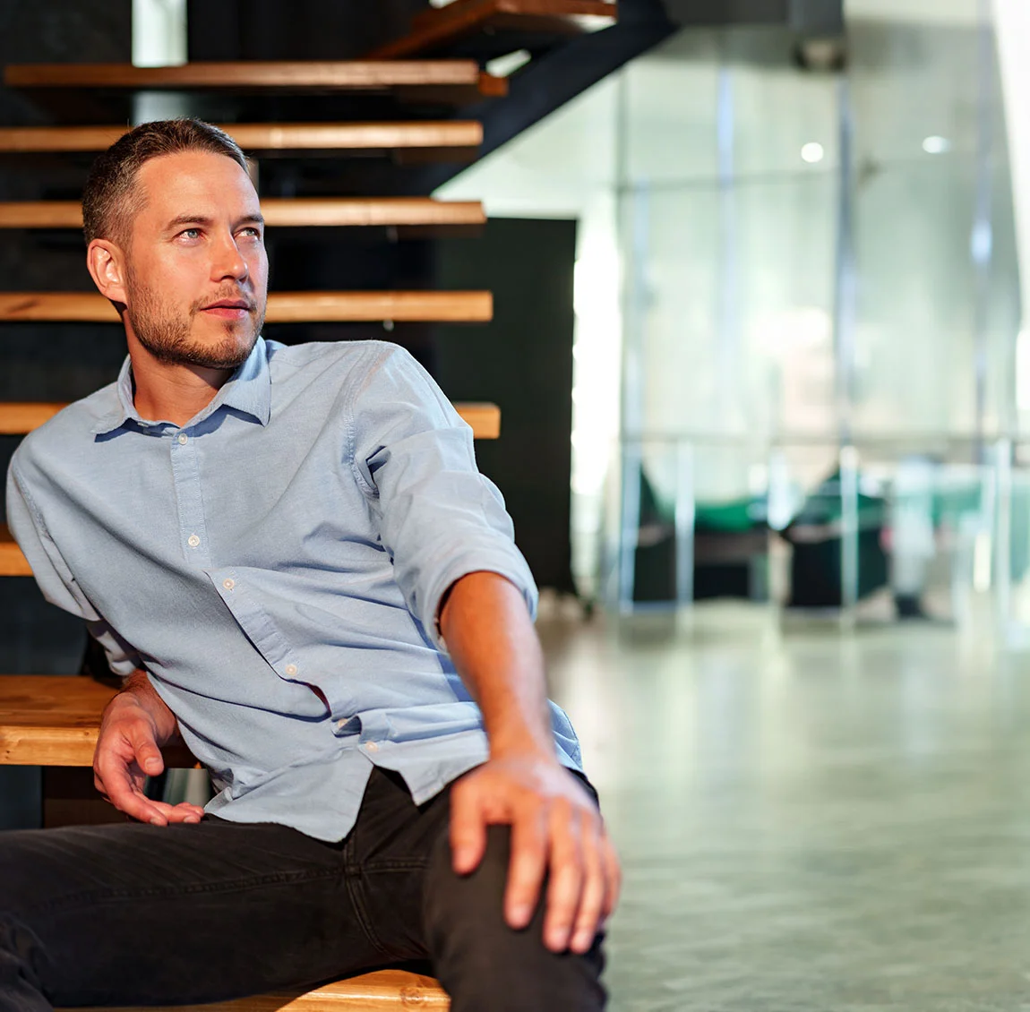 A man in a blue button up, sitting on wooden stairs - Revision Rhinoplasty at HIM Plastic Surgery