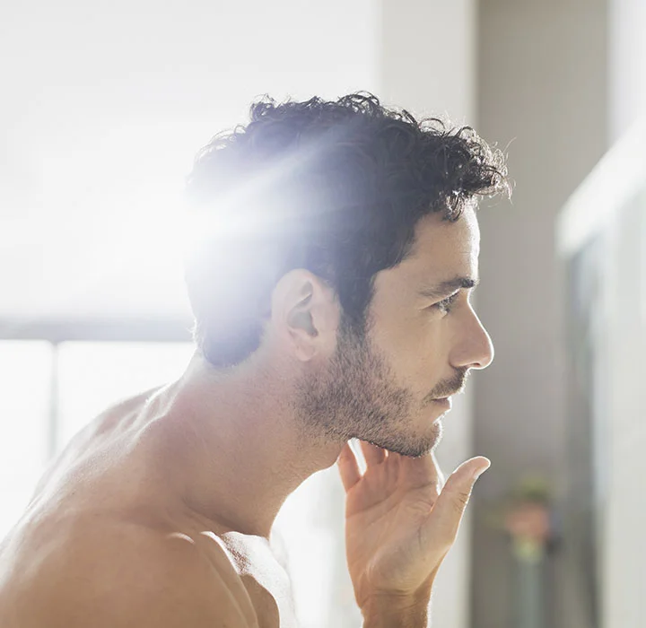 Bearded man side profile view looking in the mirror | HIM Facial Plastic Face procedures